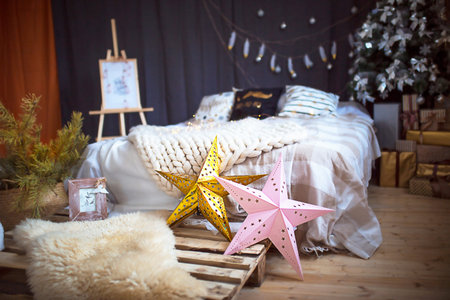 Christmas interior decor in loft style. A bed on a pallet, a large-knitted plaid, gold and pink stars, garlands, an easel. Christmas tree with gift boxes in the bedroom. New Year's moodの写真素材