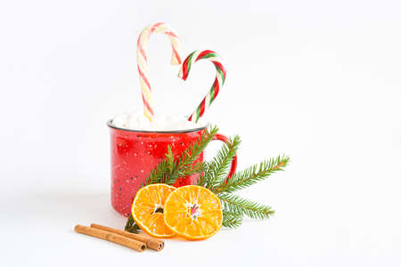 A red mug with marshmallows and candy cane in the shape of a heart is decorated with a natural fir branch or dried orange slices and cinnamon sticks. Christmas and New Year, the flavor of the holiday.の写真素材