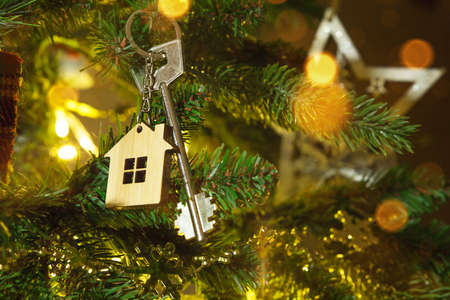 Key to the house with a keychain is hanging on the Christmas tree. A gift for New Year, Christmas. Building, design, project, moving to new house, mortgage, rent and purchase real estate. Copy spaceの写真素材