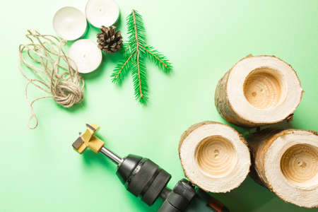 DIY Christmas candle holder made of pine logs, candles, craft rope, fir branches and cones. A drill is a tool for manufacturing. Drill holes. Step-by-step instructions flat lay, step 2.の写真素材