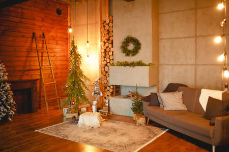 Christmas interior in the style of a Scandinavian loft: gray concrete, wooden decor, incandescent lamps, realistic artificial Christmas tree. Cozy new year in a country houseの写真素材