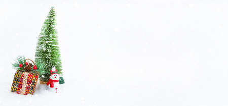 A Christmas tree, a gift box and a toy snowman on white natural snow in a snowfall. Decoration for New year and Christmas, greeting card with copyspaceの写真素材