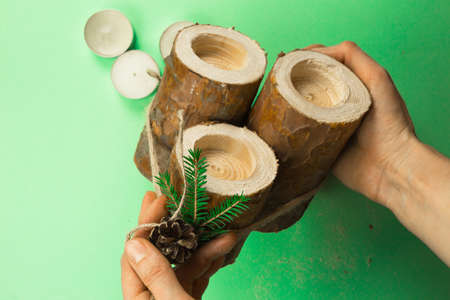 DIY Christmas candle holder made of pine logs, candles, craft rope, fir branches and cones. Hands attach the decoration. Step-by-step instructions flat lay, step 4.の写真素材
