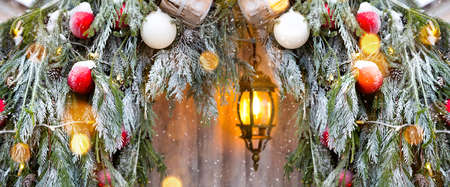 Outdoor Christmas decorations made of natural spruce branches, toys, garlands and a glowing lantern in the snow in a blizzard. Winter outside, snowfall. New Year decorの写真素材