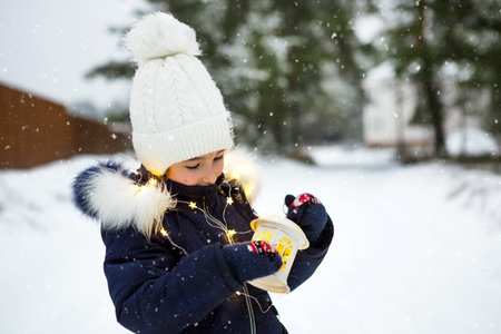 A child in winter on a snowy street under a snowfall in a glowing garland with stars. Preparation...