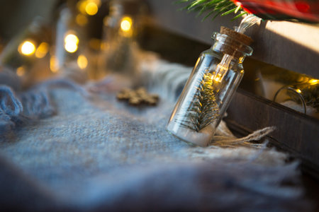 Fairy lights in a jar with a Christmas tree and snow close-up on a warm cozy plaid with wooden...