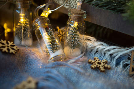 Fairy lights in a jar with a Christmas tree and snow close-up on a warm cozy plaid with wooden decor. Christmas and New Year, festive decor, comfort at home, preparation for celebration, fabulous moodの写真素材