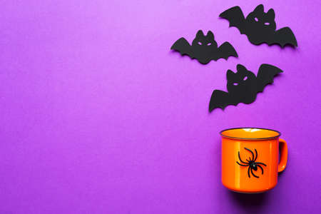 Orange mug on a purple background with terrible Halloween decorations. The concept of the Halloween holiday. Drink, fun, party. Copy space, mock up, flatlyの写真素材