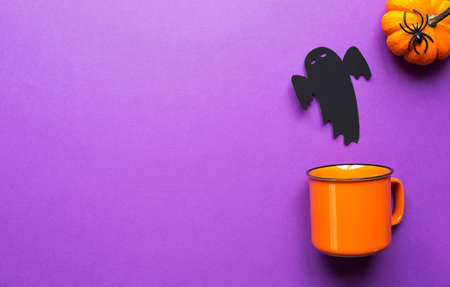 Orange mug on a purple background with terrible Halloween decorations. The concept of the Halloween holiday. Drink, fun, party. Copy space, mock up, flatlyの写真素材