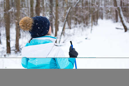 Skier in windbreaker and hat with pompom with ski poles in his hands with his back against the...