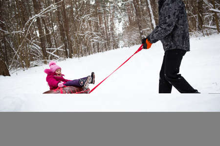 Dad rides his daughter on a tube from a slide in winter in a snowfall. Tubing, winter sports outdoor...