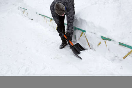 A man cleans snow with a shovel in winter in a swept yard after a snowfall. Winter weather conditions, snow shovel for car trunkの写真素材