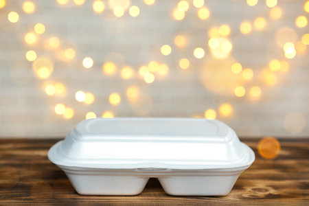 Christmas decor of food delivery service containers. New year eve promotion. Ready-made hot order, disposable plastic box in fairy light on table. Work on public holidays catering. Copy space, mock upの写真素材