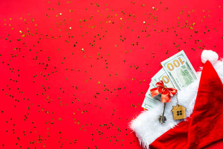 Wad of 100 dollar bills in Santa's hat on a red backgroundand House key. Christmas gift of finance, savings, wealth, expenses in new year money present. Real estate, housing, mortgage, relocation.の写真素材