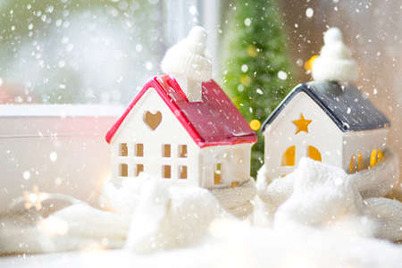 Cozy house is wrapped in a hat and scarf in a snowstorm -window sill decor for Christmas, New Year. Winter, snow - home insulation, protection from cold and bad weather, heating system. Festive moodの写真素材