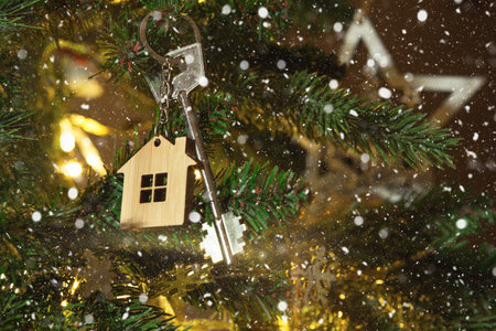 Key to the house with a keychain is hanging on the Christmas tree. A gift for New Year, Christmas. Building, design, project, moving to new house, mortgage, rent and purchase real estate. Copy spaceの写真素材