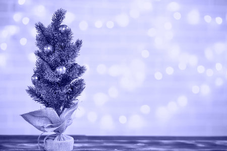A small Christmas tree stands on a table with fairy lights in bokeh. Copy space and empty space