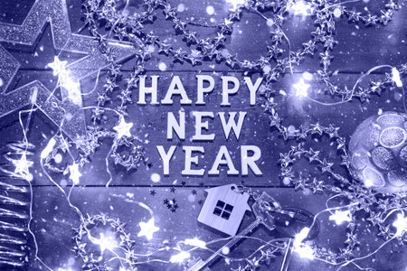 House key with keychain cottage on a festive background with sequins, stars, lights of garlands. Happy New Year-wooden letters, greetings, greeting card. Purchase, construction, relocation, mortgageの写真素材