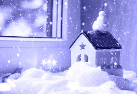 Cozy house is wrapped in a hat and scarf in a snowstorm -window sill decor. Winter, snow - home insulation, protection from cold and bad weather, room heating system. Festive mood, Christmas, New Yearの写真素材