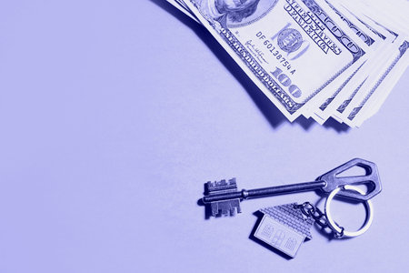 Home key with a keychain on a stack of $ 100 bills on yellow background. Purchase of an apartment, house, real estate, business, mortgage and housing loan from bank, savings, cash, moving. Copy spaceの写真素材