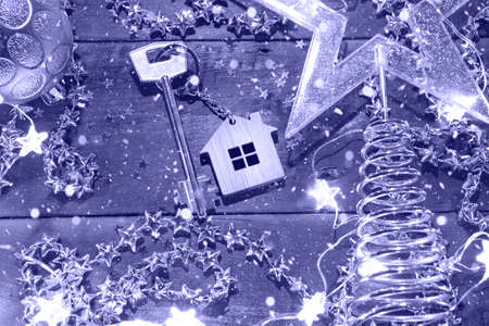 House key with keychain cottage on a festive background with sequins, stars, lights of garlands. Happy New Year-wooden letters, greetings, greeting card. Purchase, construction, relocation, mortgageの写真素材