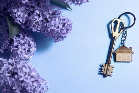 House key with keychain on blue spring background and lilac branches. Summer holiday home, booking cottage in the countryside, moving to new home, mortgage, rent and purchase real estate. Tourismの写真素材