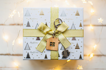 House key with keychain cottage. Happy New Year-golld bow in gift box, background with snow, fairy...
