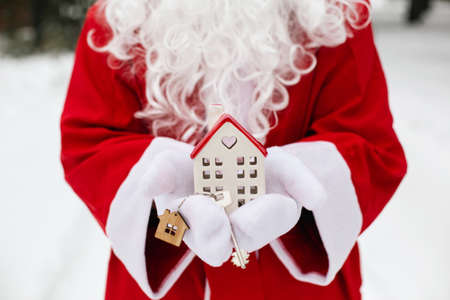 House key with keychain cottage in hands of Santa Claus outdoor in snow. Deal for real estate, purchase, construction, relocation, mortgage. Cozy home. Merry Christmas, new year booking event and hallの写真素材