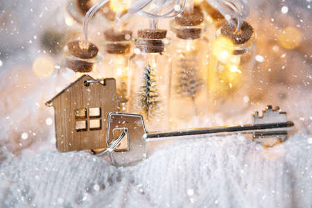 House key with keychain cottage with fairy lights in jar with Christmas tree and snow. Purchase, construction, relocation, mortgage, booking. Merry Christmas, gift, present and target in new yearの写真素材