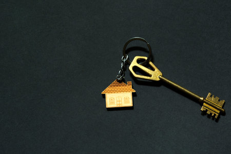 Key chain in the shape of house with key on a black background. Building, design, project, moving to new home, mortgage, deposit, rent and purchase real estate. copy spaceの写真素材