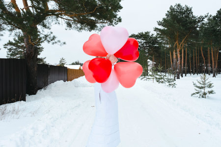 Happy woman without a face with heart-shaped balloons outdoor in winter with snow. Valentine's Day, love and infatuation, a gift from a boyfriend, a declaration of love, lifestyleの写真素材