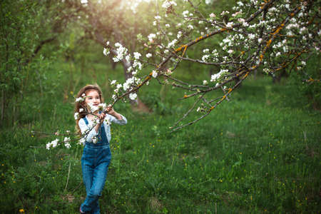 A cute little girl of 5 years old in a blooming white apple orchard in spring. Springtime, orchard, flowering, allergy, spring fragrance, tenderness, caring for nature. Portraitの写真素材