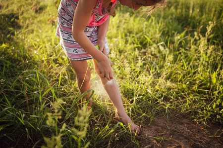 Girl sprays mosquito spray on the skin in nature that bite her hands and feet. Protection from insect bites, repellent safe for children. Outdoor recreation, against allergies. summer timeの写真素材