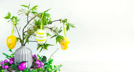 A bouquet of green branches with blooming fresh leaves in a vase on the table is decorated with colorful Easter eggs. Decor in the interior of the home for Easter. copy spaceの写真素材