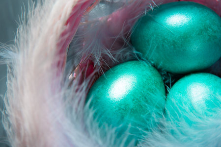 Colorful painted marble shiny Easter eggs in a basket with delicate feathers close-up. Nest with...