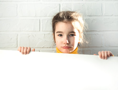 A sad girl holds a white sheet of paper - mock-up for advertising, slogan, inscription. Copy space...