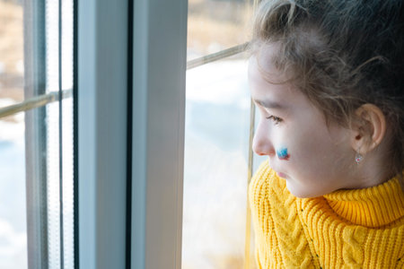 A sad child at the window with the flag of Russia, worries with tears in his eyes. Conflict between...