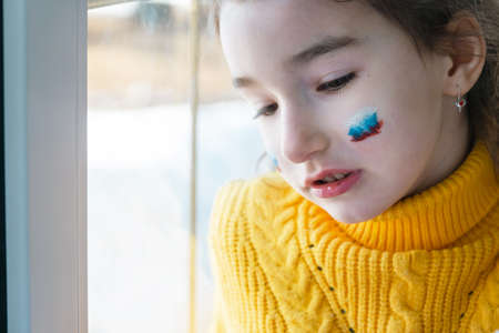 A sad child at the window with the flag of Russia, worries with tears in his eyes. Conflict between Russia and Ukraine, fearの写真素材