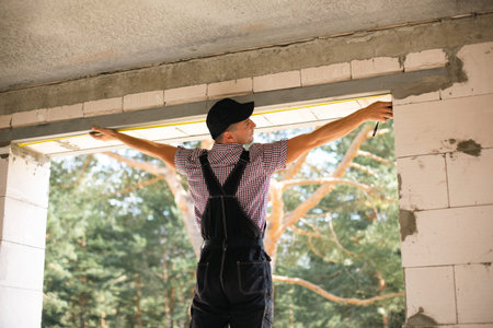 Construction worker at construction site measures the length of window opening and brick wall with...