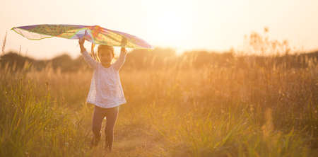 A girl runs into a field with a kite, learns to launch it. Outdoor entertainment in summer, nature and fresh air. Childhood, freedom and carelessness. A child with wings is a dream and a hope.の写真素材