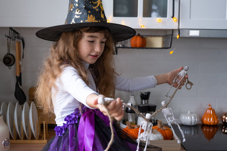 Child decorates the kitchen in home for Halloween. Girl in a witch costume plays with the decor for...