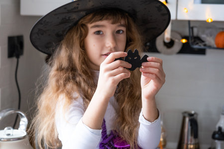 Child decorates the kitchen in home for Halloween. Girl in a witch costume plays with the decor for the holiday - bats, jack lantern, pumpkins. Autumn comfort in house, Scandi-style kitchen, loftの写真素材