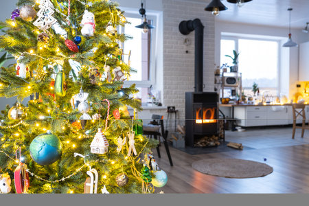 Festive interior of house is decorated for Christmas and New Year in loft style with black stove, fireplace, Christmas tree. Warm studio room with set table, burning wood, cozy and heating of homeの写真素材