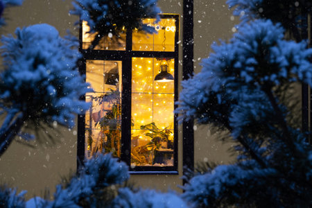 Cozy festive window of the house outside with the warm light of fairy lights garlands inside -...
