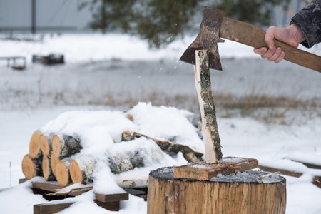 A man is chopping firewood with an ax in winter outdoors in the snow. Alternative heating, wood harvesting, energy crisisの写真素材