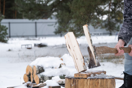 A man is chopping firewood with an ax in winter outdoors in the snow. Alternative heating, wood harvesting, energy crisisの写真素材