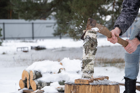 A man is chopping firewood with an ax in winter outdoors in the snow. Alternative heating, wood harvesting, energy crisisの写真素材