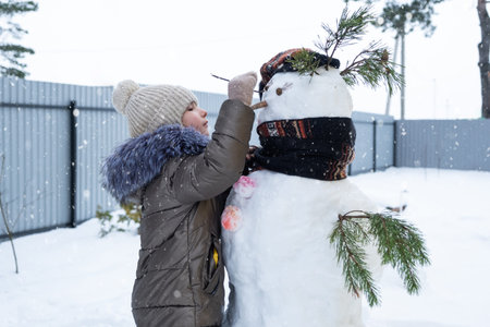 A child paints a snowman's face with paints - winter entertainment and creativity, sculpting a snowman in winter outdoor.の写真素材