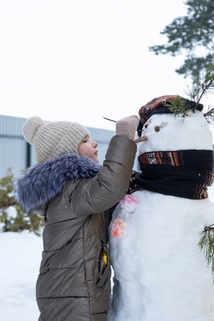 A child paints a snowman's face with paints - winter entertainment and creativity, sculpting a snowman in winter outdoor.の写真素材