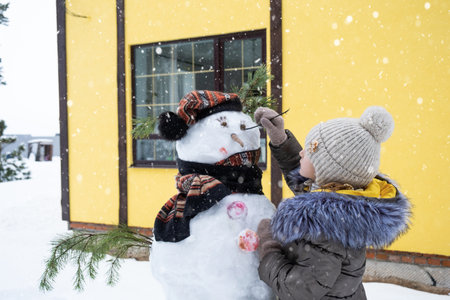 A child paints a snowman's face with paints - winter entertainment and creativity, sculpting a snowman in winter outdoor.の写真素材